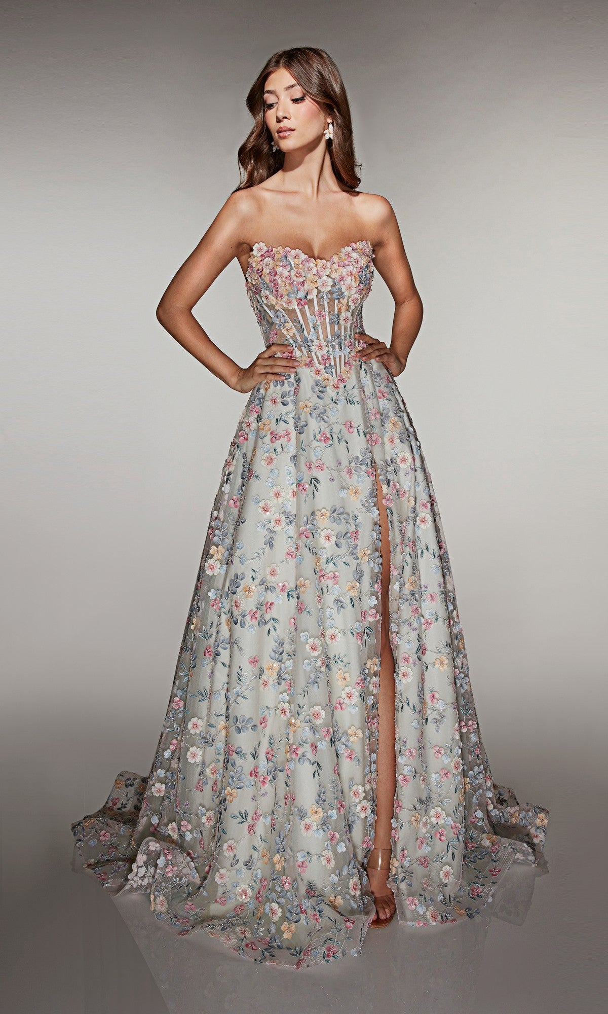 A woman in the Alyce 61986 long prom dress with a strapless neckline, 3D floral appliques, sheer bodice, high slit, and a-line skirt poses with hands on hips.